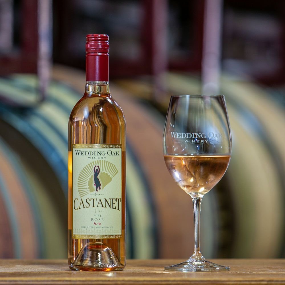 A bottle of Castanet rosé beside a glass, barrels behind